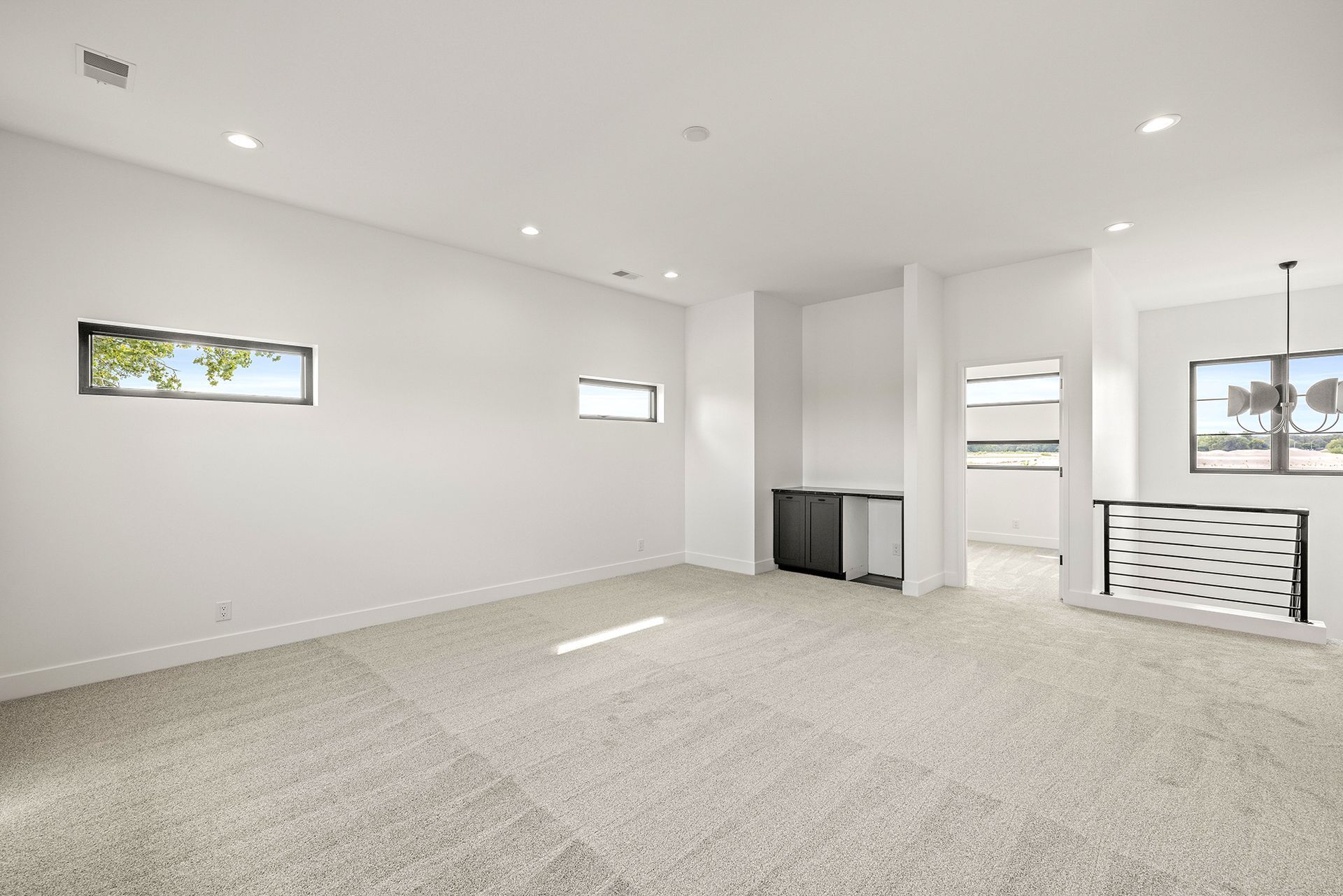 A bright, modern, minimalist room with white walls, carpeted floors, two small rectangular windows, and a wet bar area.