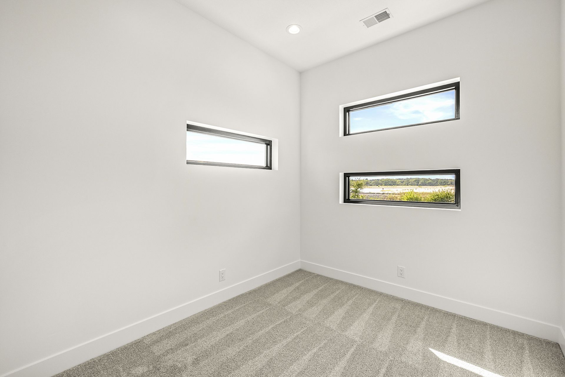 A minimalist room with white walls, gray carpet, and three horizontal rectangular windows.