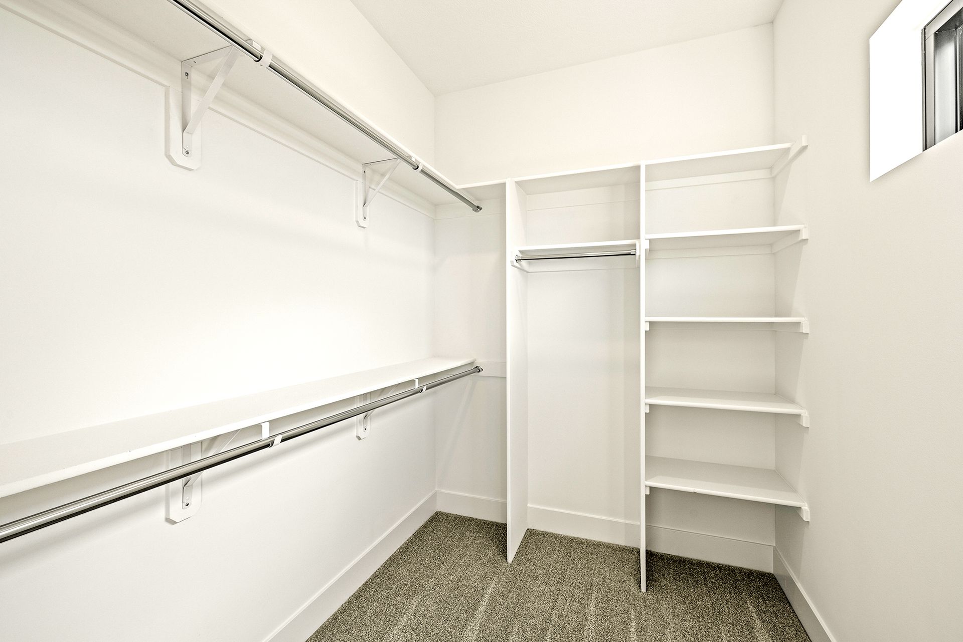 An empty walk-in closet with white walls, white shelving, a hanging rod, and patterned carpet flooring.