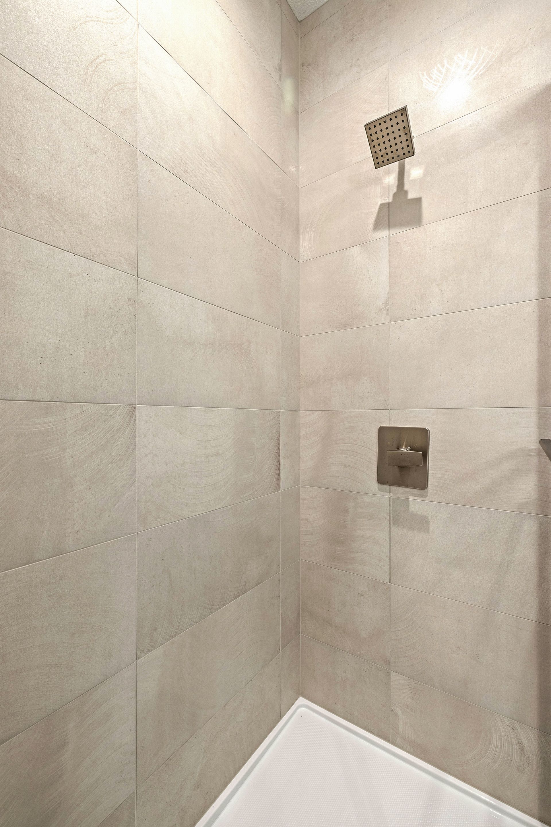A walk-in shower with light beige tiled walls, a square overhead shower head, and a matching wall-mounted control handle.