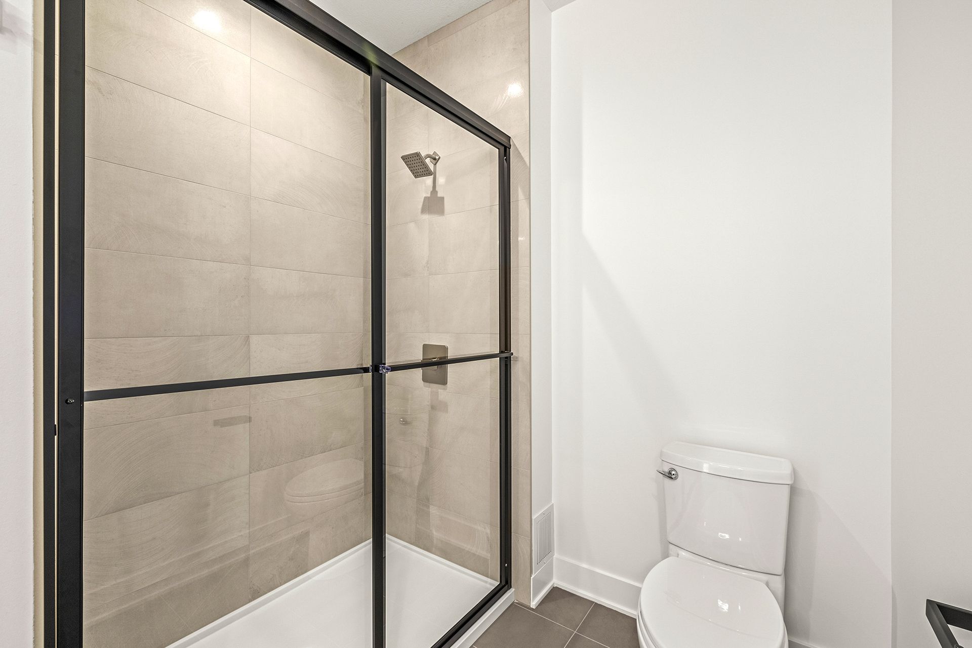 A modern bathroom with a glass-enclosed tiled shower next to a white toilet.