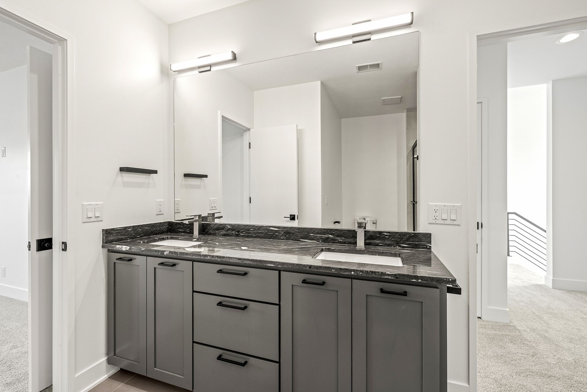 A modern bathroom with a dual-sink vanity, dark grey cabinets, dark stone countertop, and a large mirror.