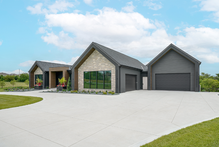 Modern house with gray and tan exterior, black roof, and large windows on a sunny day.