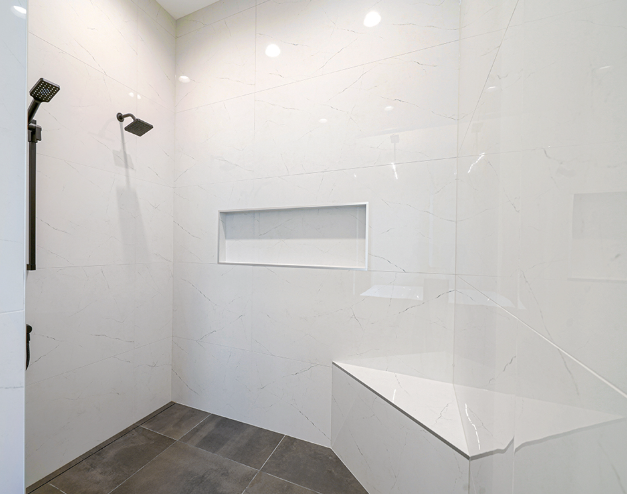 White tiled shower with a built-in bench and recessed shelf. Dark shower fixtures.