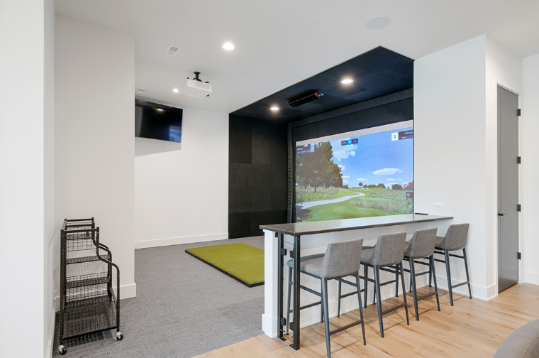 Golf simulator room with screen, bar seating, and golf mat.