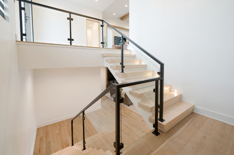 Staircase with wooden steps and black metal railings, leading up to a landing with glass panels.