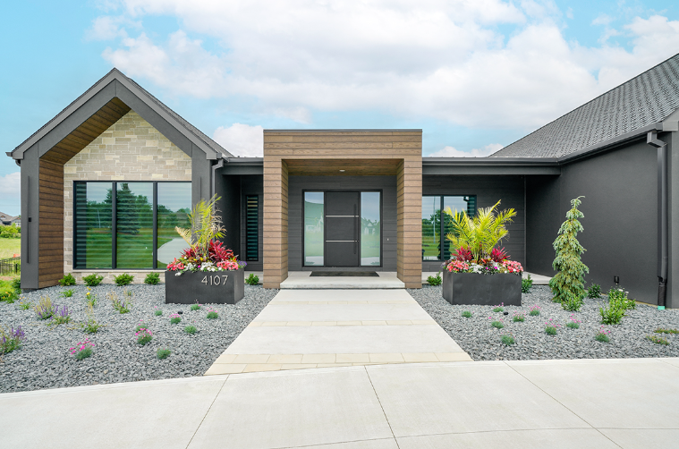 Modern gray house exterior with concrete walkway, flower boxes, and a blue sky.