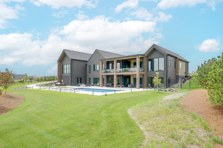 Modern gray house with pool and expansive green lawn on a sunny day.