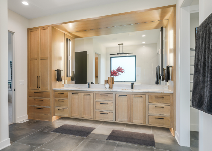 Modern bathroom with light wood cabinets, large mirror, and black accents.