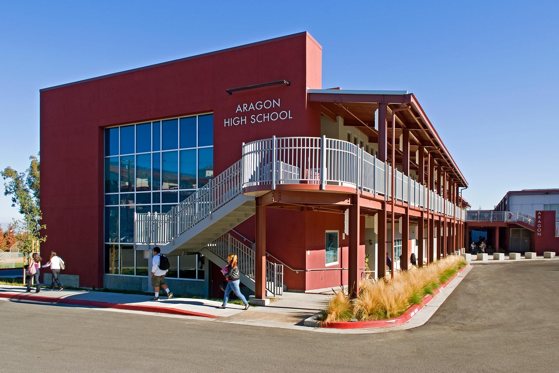 Aragon High School building with red exterior and students walking outside on a sunny day.