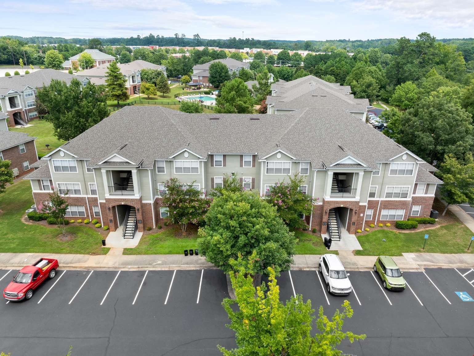 Apartment complex with brick accents, gray roof, and parking lot. Cars parked in front of building.