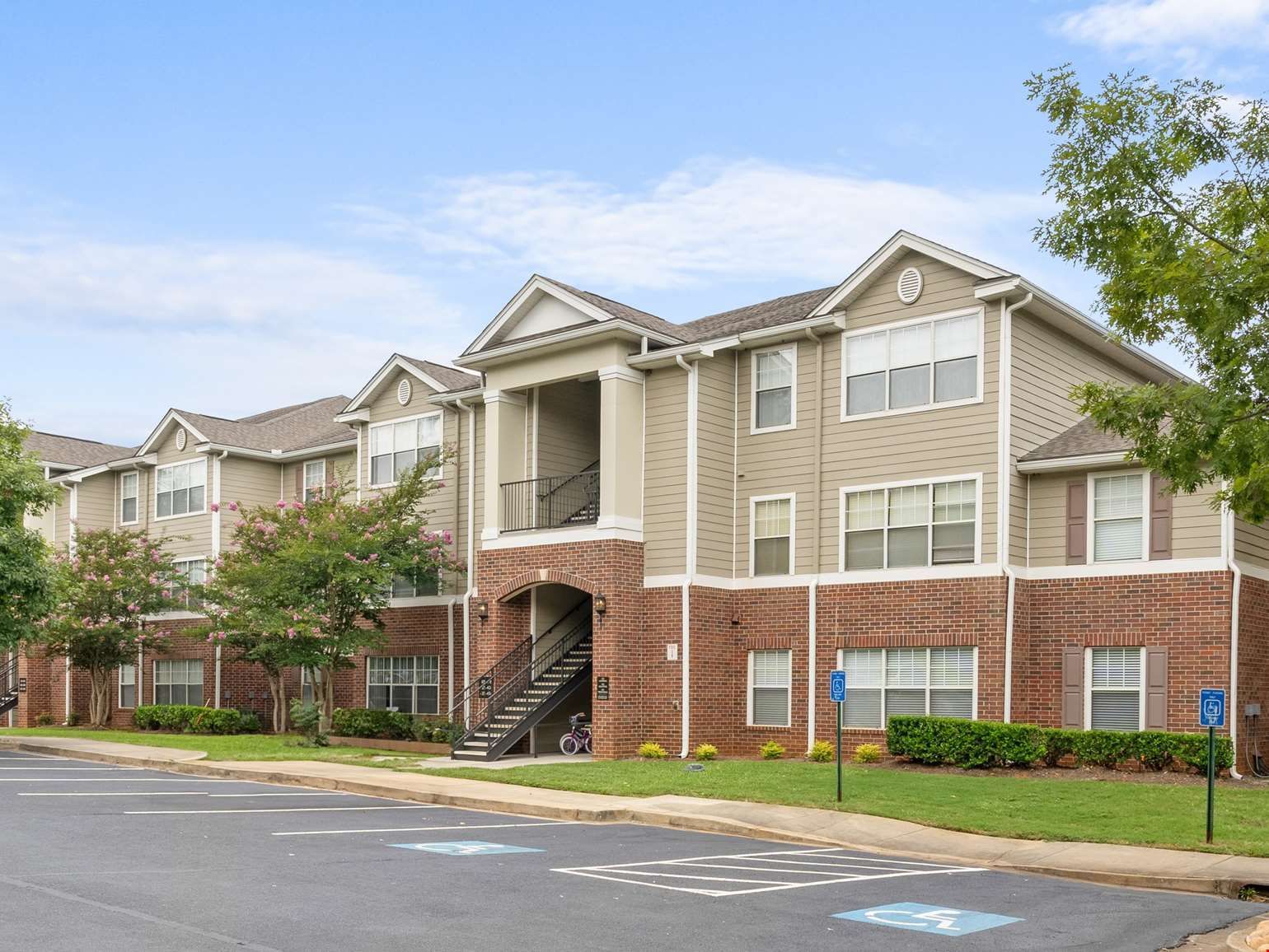 Apartment building with brick facade, beige siding, and accessible parking spaces on a sunny day.