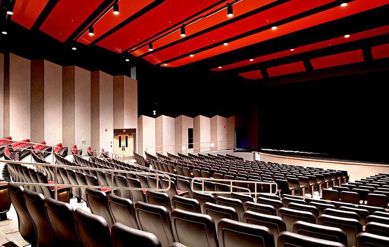 An empty auditorium with rows of black seats facing a black stage; red ceiling.