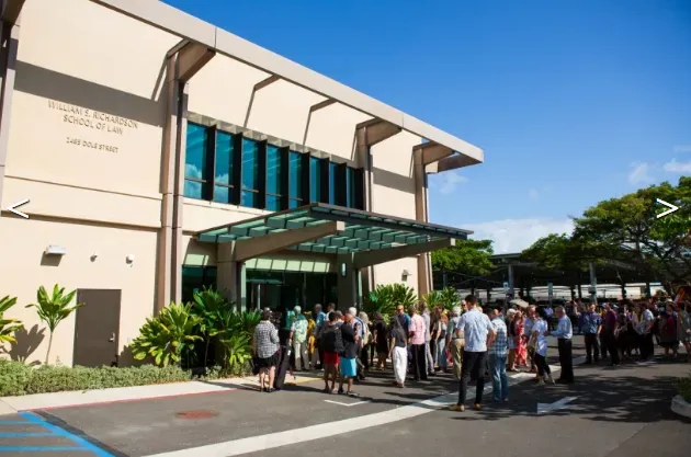 People gathered outside a tan building with a sign that reads 