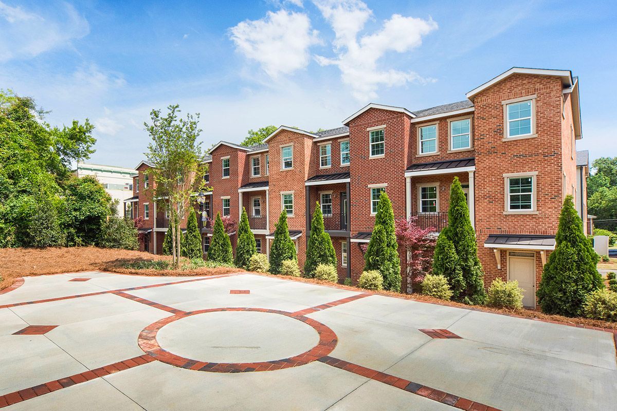 Brick townhouses with balconies, red and gray paved drive under a blue sky.