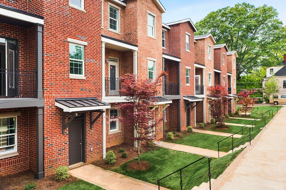 Row of brick townhouses with small balconies, green lawns, and a sidewalk.