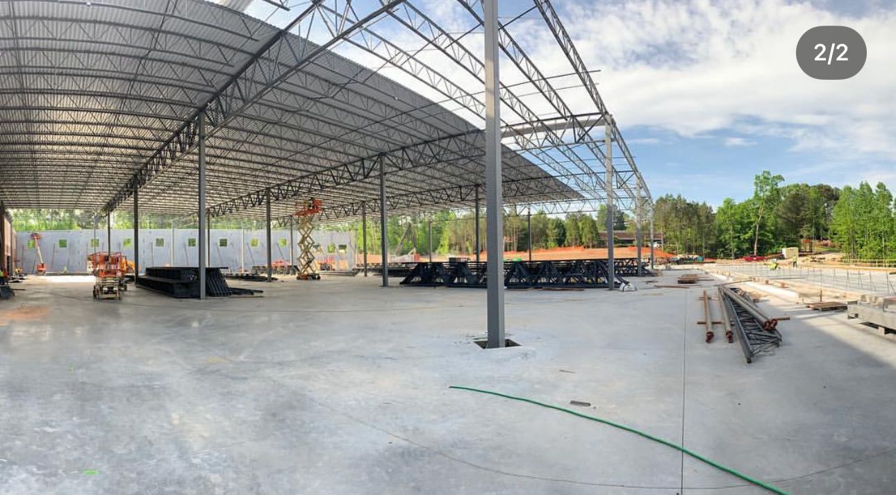 Construction site: large metal structure with a concrete floor, workers, and materials.