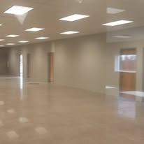 Empty, beige-walled room with square ceiling lights and a shiny floor; a door is visible.