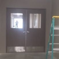 Double brown doors with rectangular windows, a ladder on the right, person visible through the window.