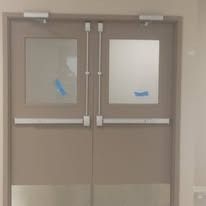 Double beige exit doors with horizontal push bars, glass windows, and metal kick plates.