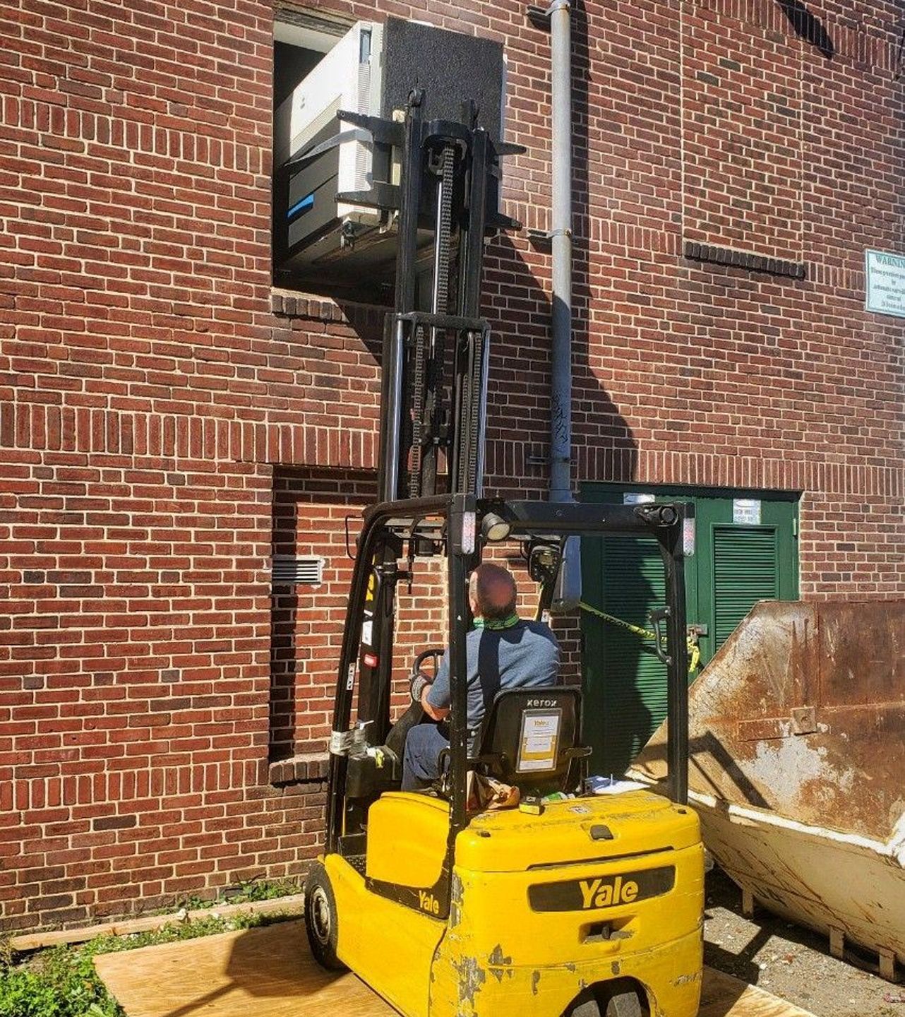 A yellow forklift is parked in front of a brick building