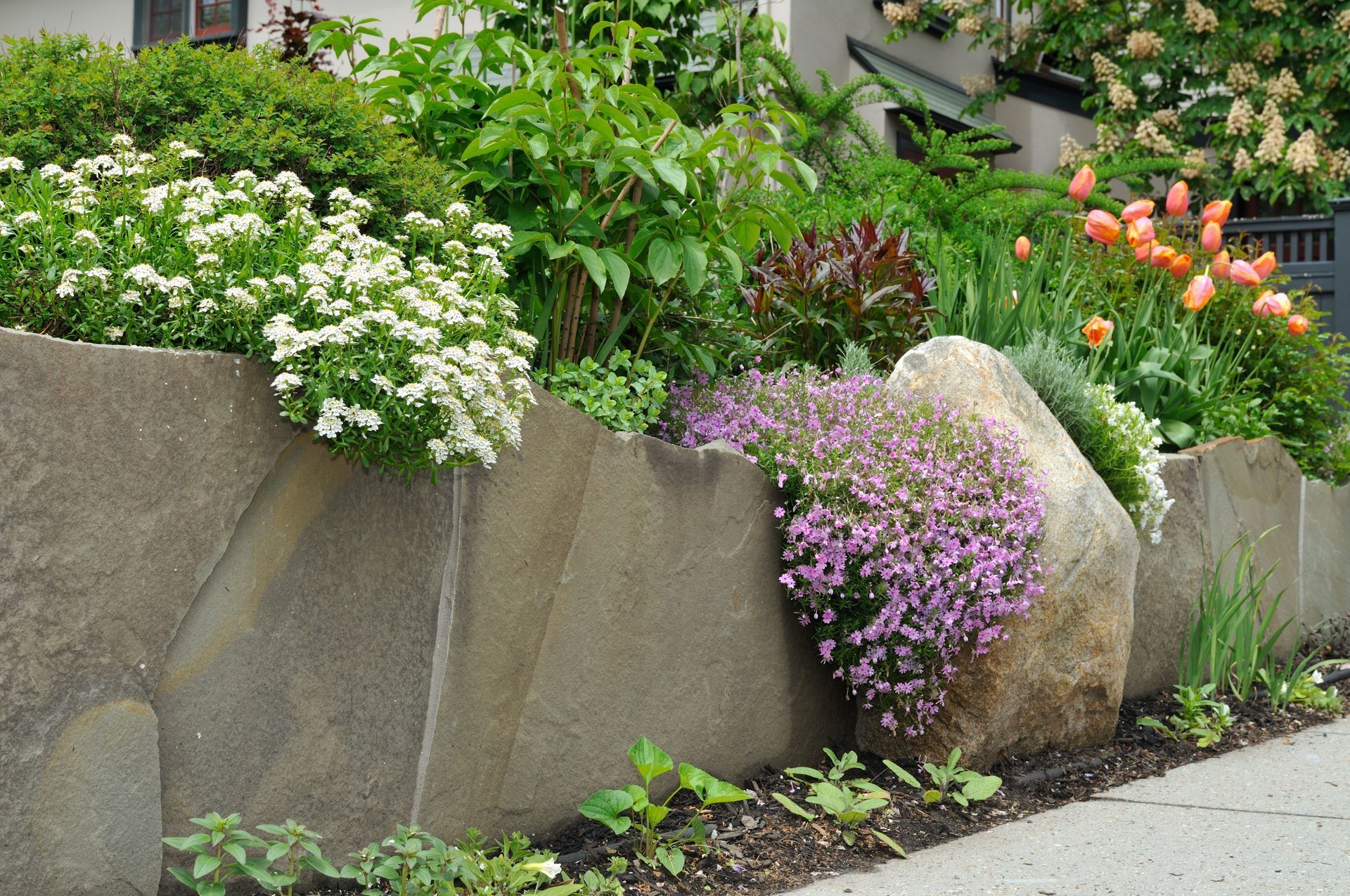 Stone retaining wall with blooming flowers of white, pink, and orange.