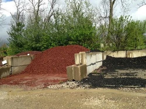 Piles of red and black mulch separated by concrete blocks. Green trees in background.