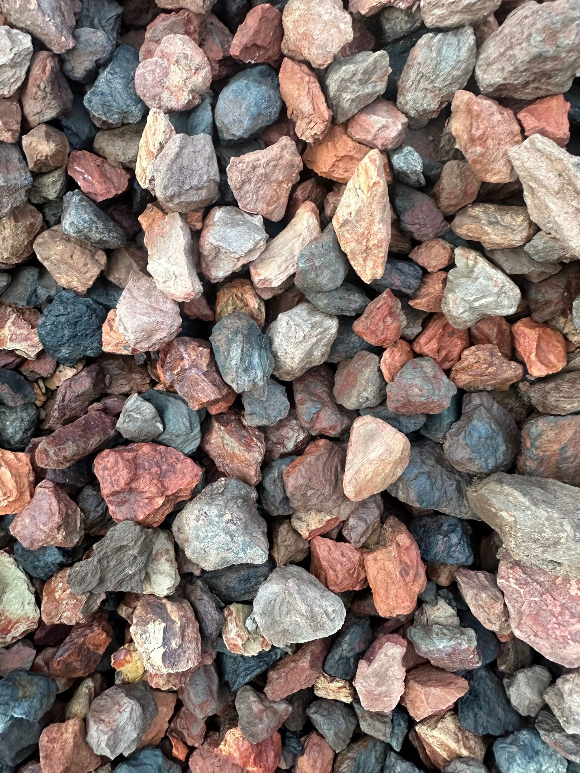 Pile of mixed, colorful landscaping rocks, including red, gray, and brown hues.