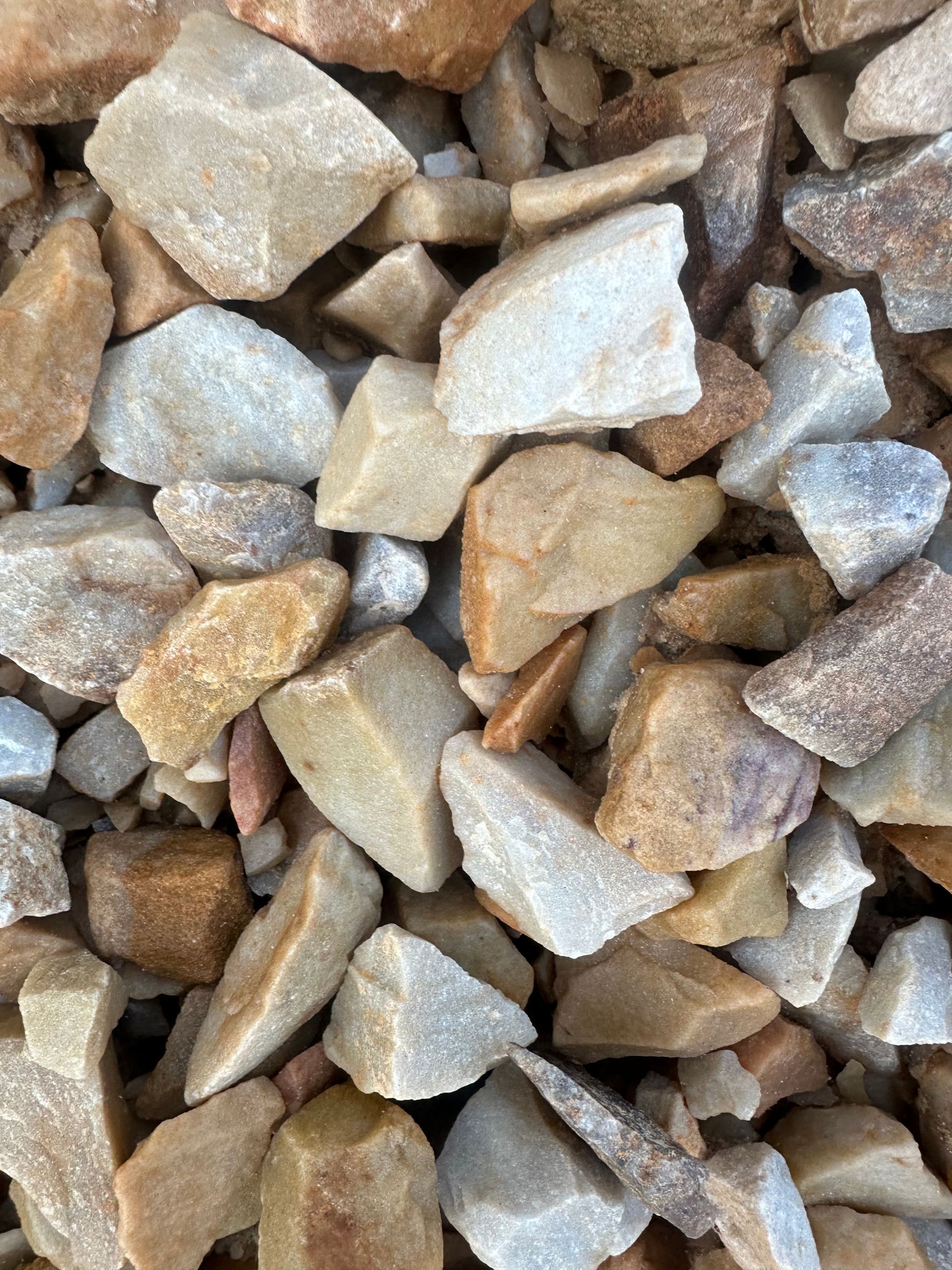 Close-up of mixed-color landscaping gravel: tan, brown, beige, and gray, angular and irregularly shaped.
