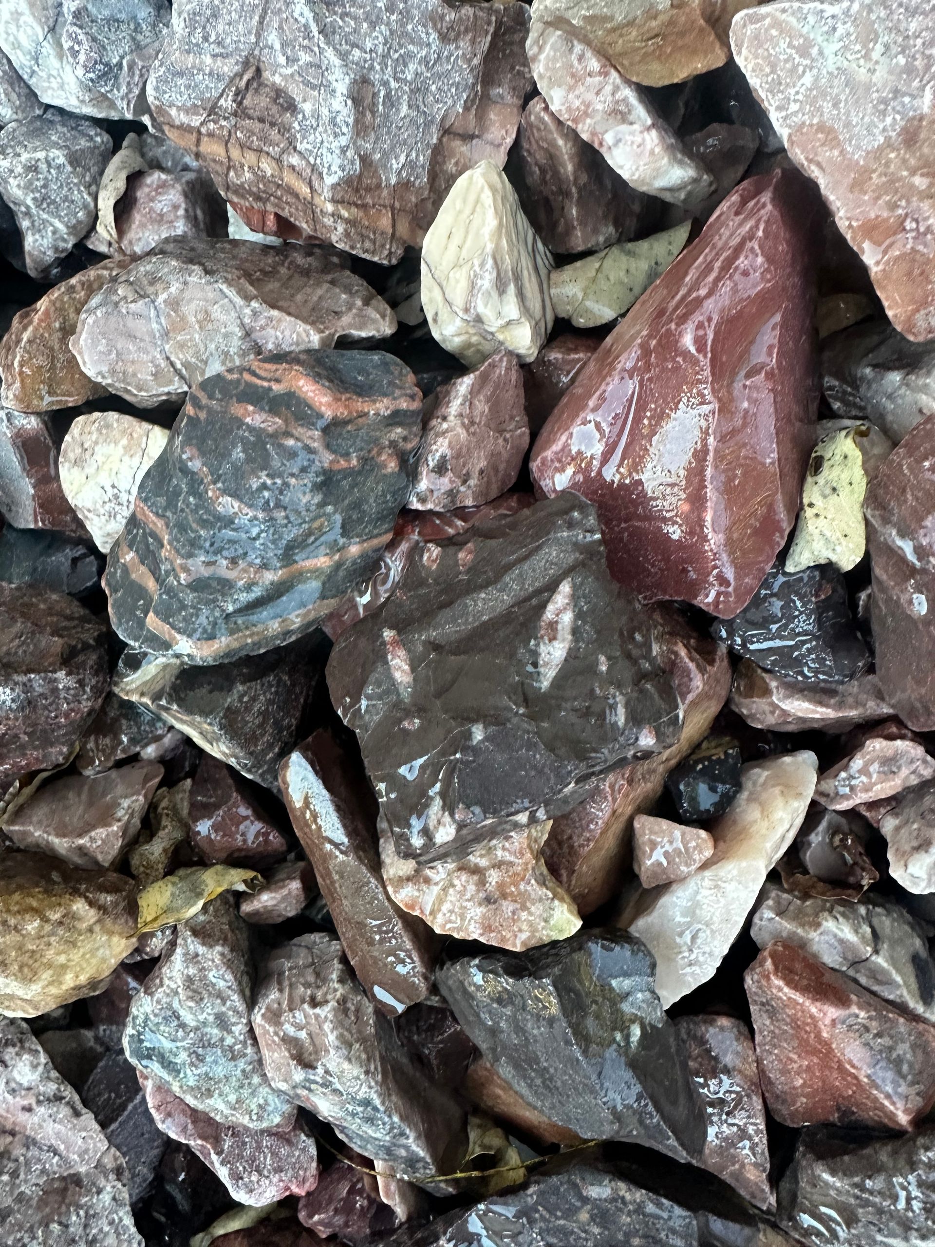 Pile of colorful rocks, red, brown, and black, with varying textures and shapes.