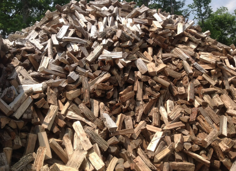 Pile of split firewood, various shades of brown and tan, in an outdoor setting.