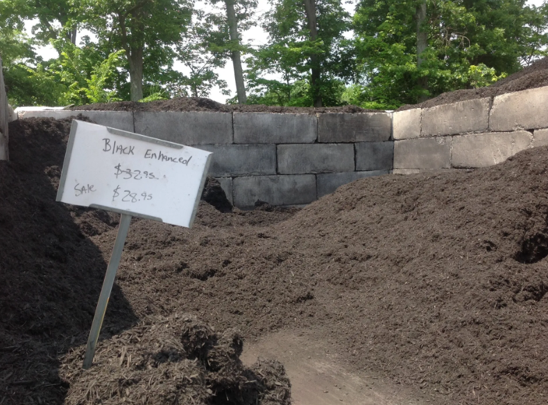 Pile of black mulch with price sign in front of a concrete retaining wall.