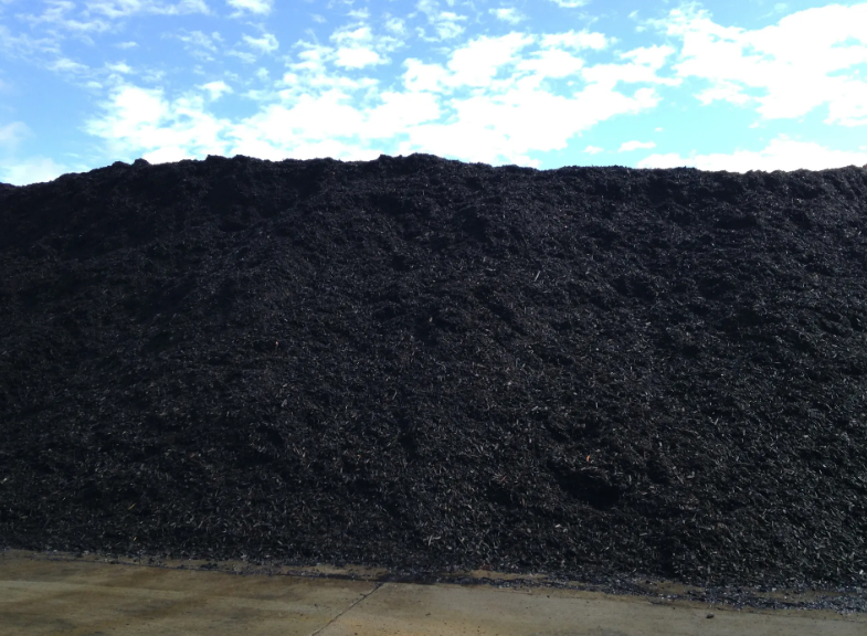 Large pile of black material, possibly shredded tires, against a blue sky with clouds.