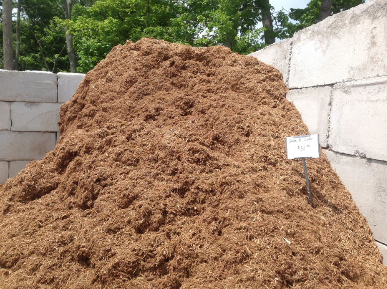 Pile of brown shredded wood chips against a cinder block wall, outdoors.