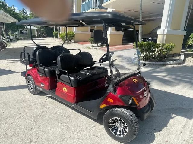 Red golf cart parked outdoors by a building in bright sunlight