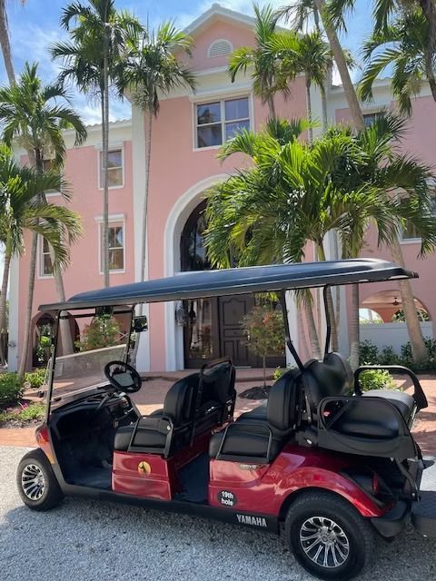 Red golf cart parked in front of a pink building with palm trees and a white archway