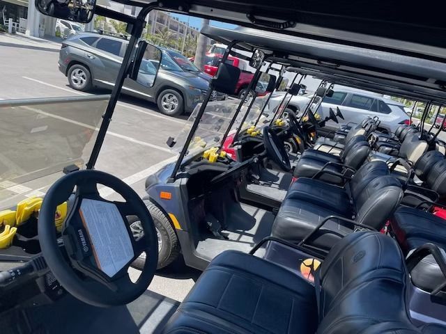 Open-air shuttle cart with rows of black seats parked in a lot, seen from the front seat.