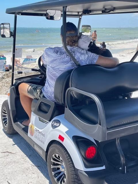 Person riding a white golf cart on a sunny beach with the ocean in the background