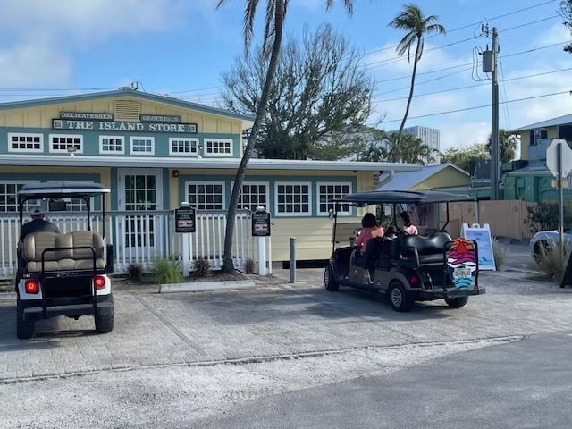 Golf carts parked outside a pale yellow building with a blue roof on a sunny day.