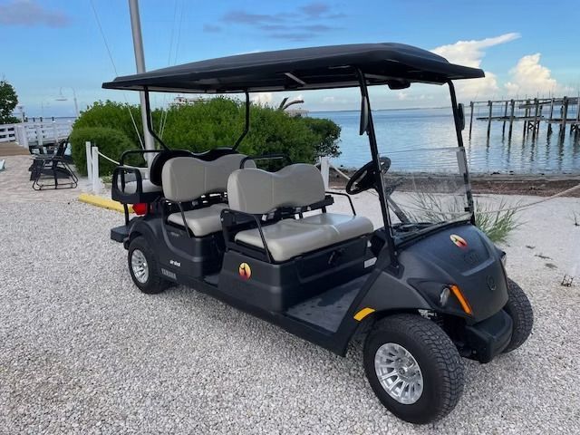 Black golf cart with canopy parked on gravel by a waterfront dock.