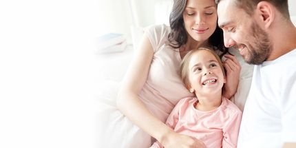 Smiling family, parents and child, are close together. The child is laughing, looking up.