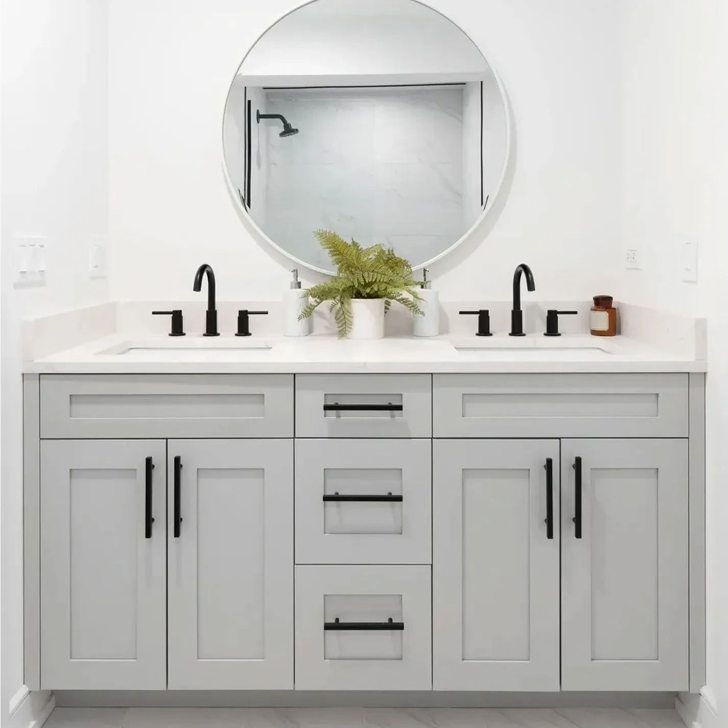 Light gray bathroom vanity with black hardware, round mirror, and two sinks.