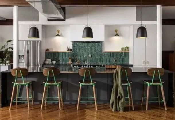 Modern kitchen with island, pendant lights, green stools, and a green tile backsplash.