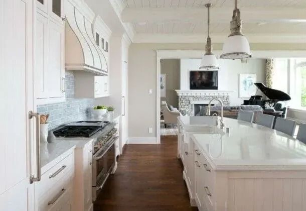 White kitchen with island and connected living room, featuring a piano and fireplace.