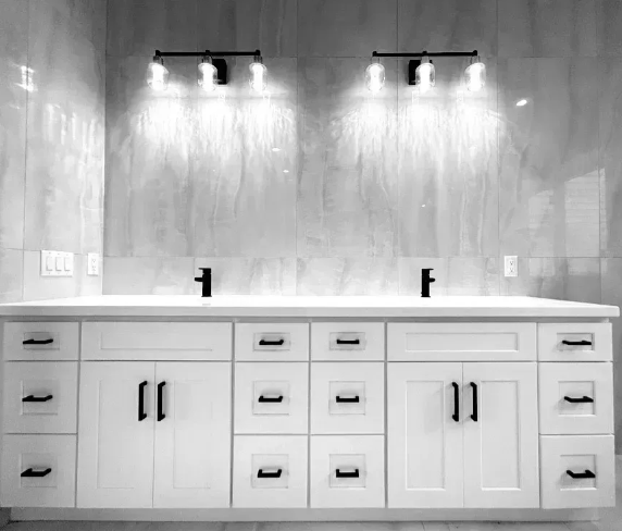 White bathroom vanity with two sinks, black hardware, and sconce lighting.