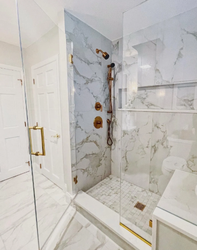 Modern bathroom with marble tile, gold fixtures, and glass shower enclosure.