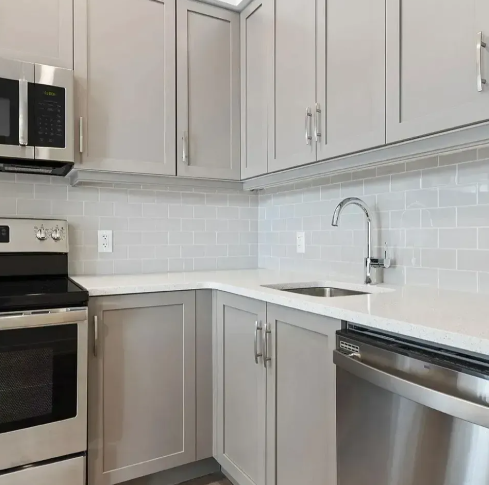 Modern kitchen with gray cabinets, stainless steel appliances, and light gray backsplash.