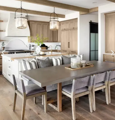 Elegant kitchen with island seating and dining table. Neutral tones, pendant lights, wooden cabinets, and modern furniture.