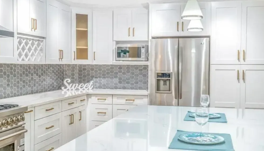 White kitchen with stainless steel refrigerator, white cabinets, and island.