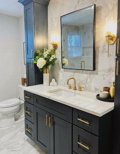 Bathroom with dark blue vanity, gold fixtures, marble backsplash, and large mirror.